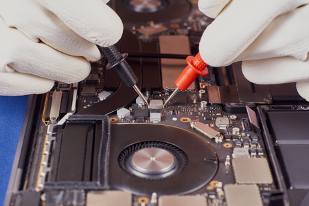 Master in the white gloves carries out diagnostics with the probes of tester. Laptop in an aluminum case on a blue velvet background. Close-upの写真素材