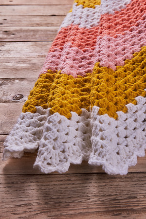 Needlework. Colorful woolen crocheted bedspread on a wooden background. Close-up.