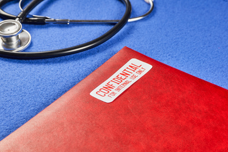 Red folder with the words Confidential for internal use only, next to phonendoscope on a blue velvet...