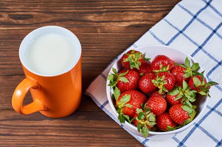 strawberry in a white bowl on napkin with mug of milk cream on wooden backgroundの写真素材