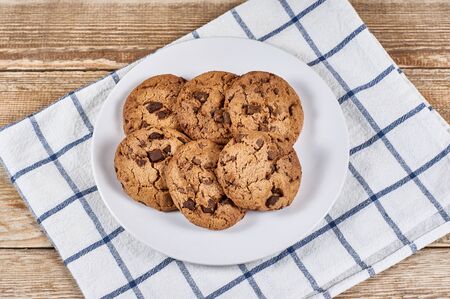 oatmeal cookies with chocolate slices in white plate and napkin on a wooden background
