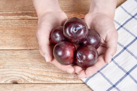 female hands holds few red plums next to a doily with figure on a wooden backgroundの写真素材