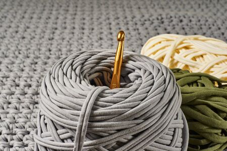 skeins of colored knitted yarn and a crochet hook against the background of a knitted carpetの写真素材