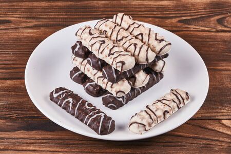Long sticks shortbread cookies in dark and white chocolate icing on a white plate on wooden...