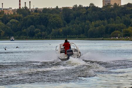 Speedboat with two people floats on the river against the background of the cityscape