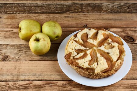 Baked apple pie on a white plate next to three green apples on a wooden backgroundの写真素材