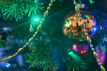 New Year's composition, Christmas decorations. Golden christmas ball hanging on a fir-tree against the background of a luminous Christmas garlandの写真素材