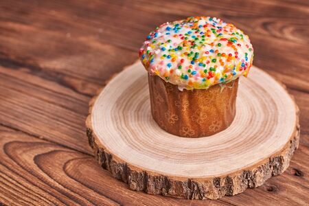 Easter composition. Easter cake on a stand made of a slice wood on a dark wooden background. With...