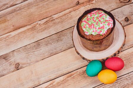 Easter composition. Easter cake on a stand made of a slice wood next to colorful Easter eggs on a...