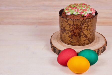 Easter composition. Easter cake on a stand made of a slice wood next to colorful Easter eggs on a...