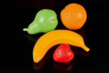 Plastic fruits on a dark background. Plastic banana, pear and strawberryの写真素材