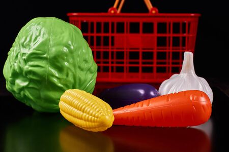 Plastic vegetables lie next to a red basket on a dark backgroundの写真素材