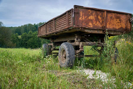 Abandoned old cargo trailer stands in a field on green grass. Close-up