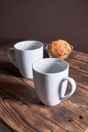 Two white empty cups and oatmeal cookies on a dark wooden backgroundの写真素材