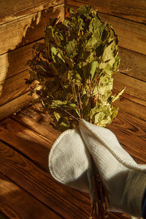 Bath supplies. A man in a mitten holds a birch broom in his handの写真素材