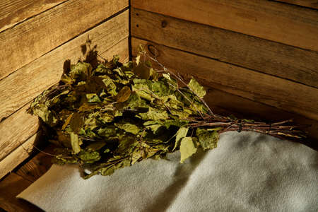Bath supplies. Birch broom lies on a litter on a wooden bench in a steam roomの写真素材