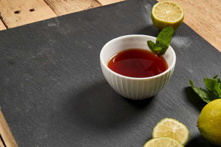 Tea in a white mug stands on a stone panel next to marshmallows and lime. There are pieces of spice for teaの写真素材