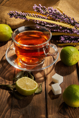 Tea in a white cup next to lime and flowers on a wooden backgroundの写真素材