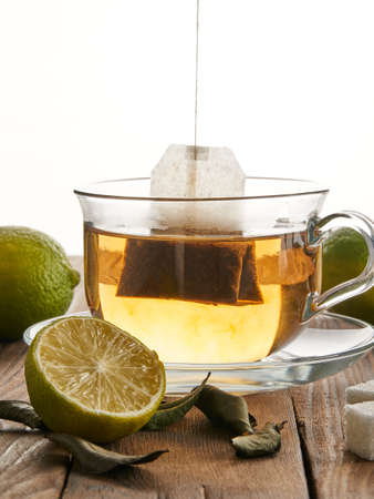 Tea in a transparent cup next to a tea bag, lime and sugar on a wooden background. Initial degree of tea brewingの写真素材