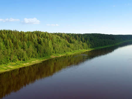 A river, a forest on a hill reflecting in water and a blue skyの写真素材