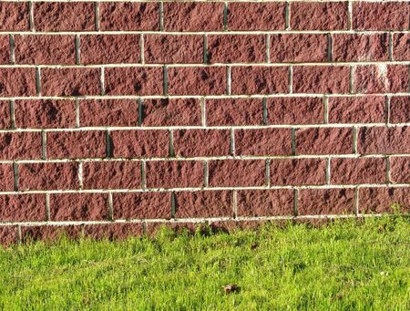 A background of a rose stone wall and green grassの写真素材