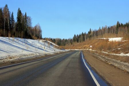 A colorful winter road with a turn and a road sign to use as a generic backgroundの写真素材