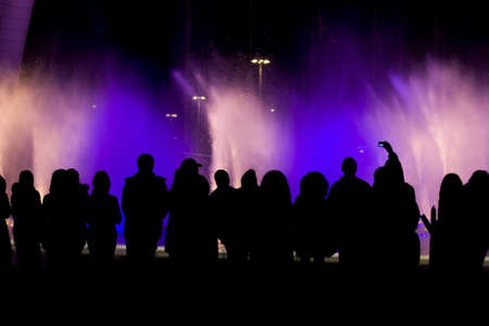 Black silhouettes of people watching a fountain showの写真素材
