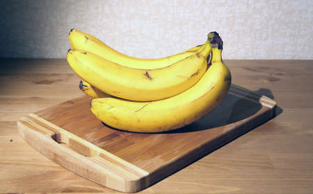 A bunch of ripe yellow bananas on a cutting board in a rustic kitchen environmentの写真素材