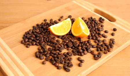 A pile of coffee beans on a board with a couple of orange lobulesの写真素材