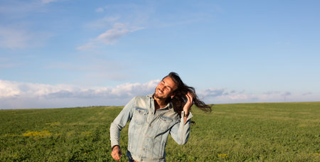 Young woman with long hair and blue jeans shirt on the green fieldの写真素材