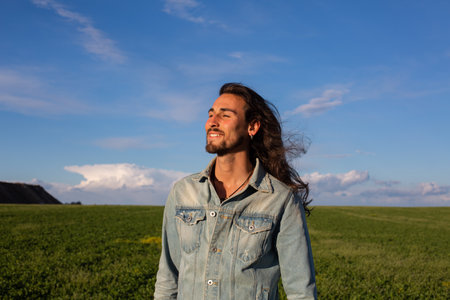 Portrait of a handsome young man with long wavy hair standing in the fieldの写真素材