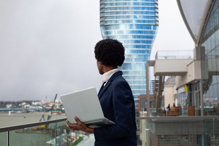 Young african american businesswoman using laptop while standing in front of modern buildingの写真素材
