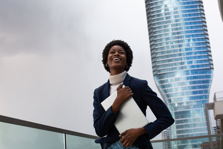 Full length portrait of a smiling african american businessman holding laptop and looking awayの写真素材