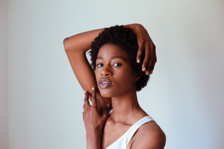 Portrait of a young african woman scratching her neck against grey backgroundの写真素材