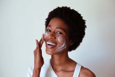 Portrait of a smiling woman applying cream on her face against grey backgroundの写真素材