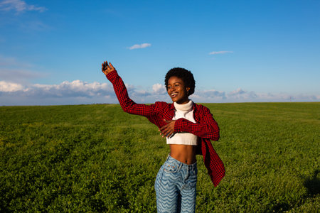 Young african american woman in checkered shirt and blue jeans on green fieldの写真素材