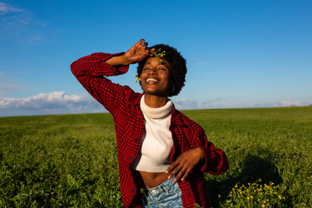 young happy and beautiful black African American woman in red shirt and jeans posing cheerful on green field smiling cheerful and confident having fun enjoying nature outdoorsの写真素材