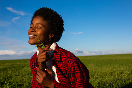 young african american woman holding a rose in a green fieldの写真素材