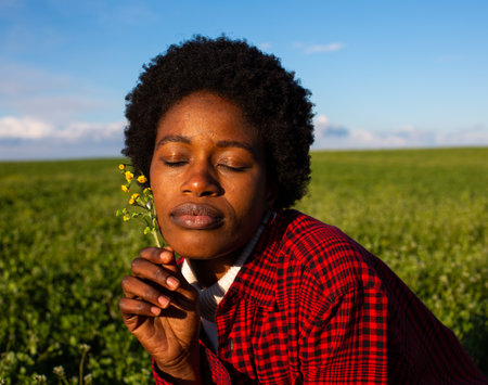 young african american woman smelling a wildflower in the field