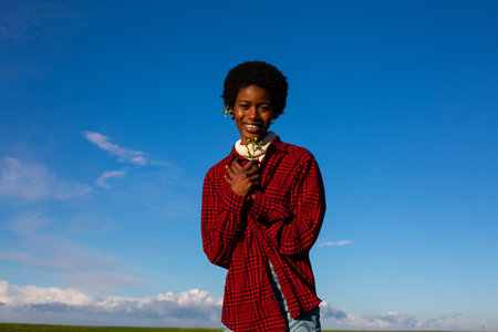 Young african american woman in red checkered shirt with flower in hand.の写真素材