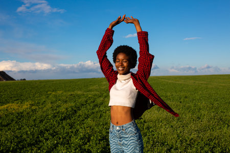 Young african american woman with arms outstretched in green field