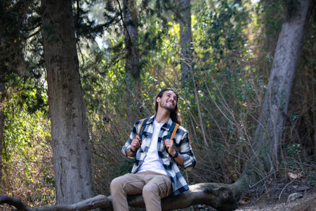 Handsome young man with backpack sitting on a log in the woodsの写真素材