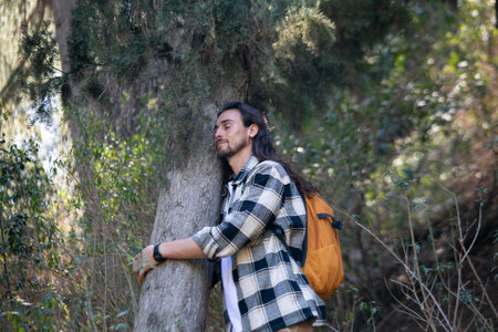 Young man with a backpack leaning against a tree in the forest.の写真素材