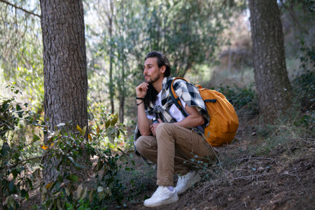 Handsome young man with backpack sitting on the ground in forestの写真素材