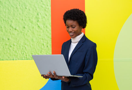 Young african american businesswoman using laptop in front of colorful wallの写真素材