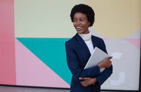 Portrait of smiling african american businesswoman holding laptop in officeの写真素材