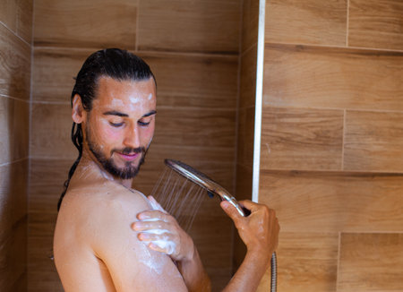Young man in the shower washing his hair with a shower head.の写真素材