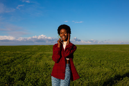 Young african american woman in checkered shirt and jeans posing on green fieldの写真素材