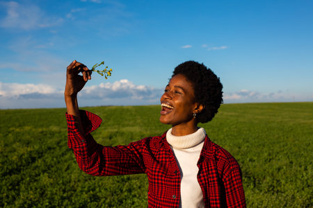 young african american woman in checkered shirt holding flower in field