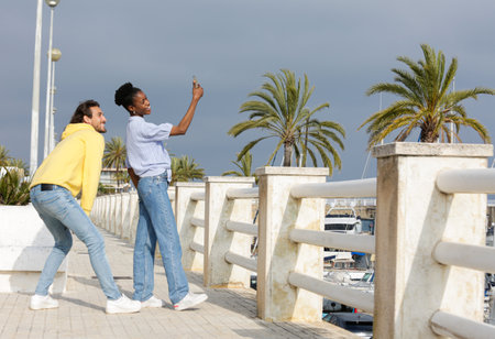 Happy young couple taking selfie with mobile phone while standing on promenade